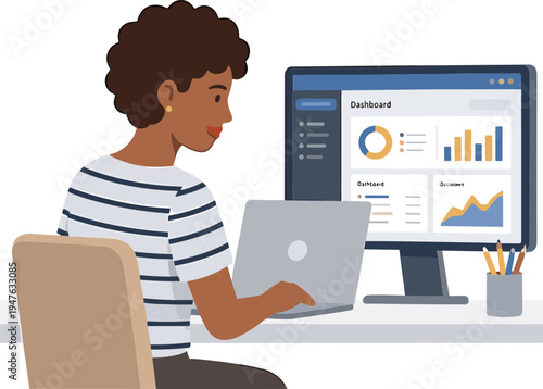 A person works on a laptop next to a large computer monitor displaying graphs in an office.
