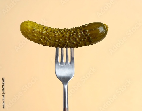 A pickle on a fork against a peach background