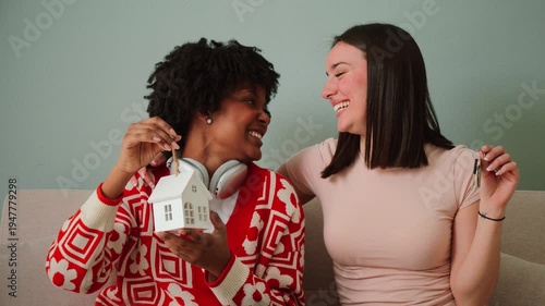 Two joyful friends celebrating their achievement of homeownership while happily holding house keys in their hands. They are excited and embracing the moment of this significant milestone in their