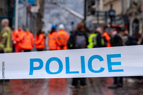 Φωτογραφία Police cordon tape in the foreground, with blurred emergency responders on a city street