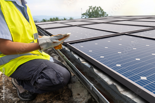Solar energy technician monitoring photovoltaic system on rooftop with mobile device