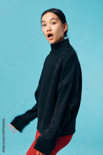 Fotografie Young woman with surprised expression wearing black sweater and red pants standing against light blue background