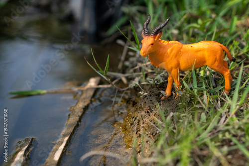 Image of a toy antelope on a riverbank. The antelope appears to be waiting for prey against the backdrop of the river and a log above the water.