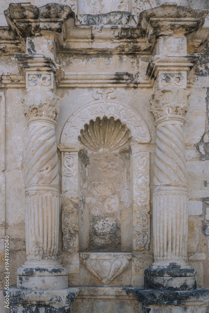 Fototapeta premium Ornate carved stone niche with spiral columns and decorative shell motif on the historic façade of the Alamo mission in San Antonio, Texas, showing weathered Spanish colonial architectural details.