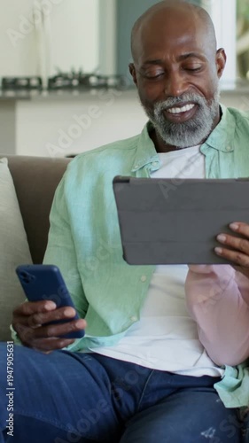 Vertical video: Tapping older man with blue phone, tablet on couch as partner entering to view