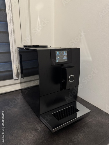 A modern kitchen interior featuring a black countertop and a black coffee machine. A modern coffee machine with a touchscreen display in a stylish kitchen interior.