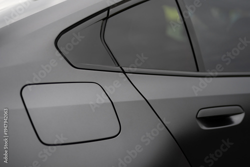 Close-up of the rear quarter panel, fuel door, and window trim of a matte grey car