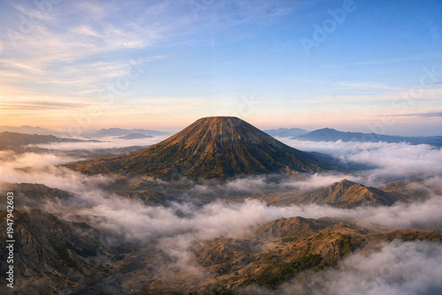 Symmetrical volcano above misty hills in golden sunrise light
