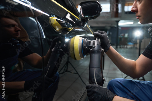 Experienced detailer is polishing motor vehicle body with orbital buffer
