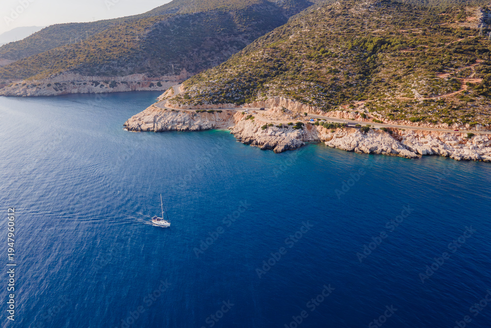 Fototapeta premium White sailboat cruising through blue sea along shore, aerial view
