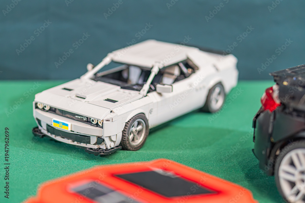 Fototapeta premium Two Lego toy cars on a textured, green-brown surface, with a white Lego car compact design, black tires, cockpit detail slightly ahead and a streamlined dark car t - Kyiv, Ukraine - June 7, 2025