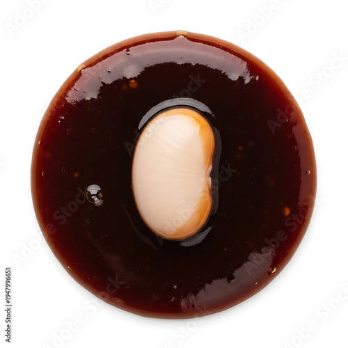A single white bean submerged in a dark, rich, glossy sauce from a top view