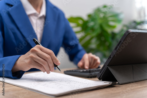 Close up of Asian female teacher hands holding pen while checking student exam papers,Recording scores on tablet and uploading academic data to central online system, Fast digital education management