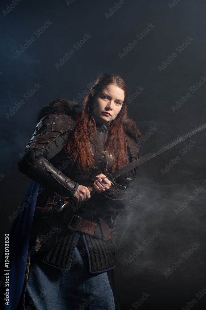 Fototapeta premium A fierce warrior woman with fiery hair and armor holds a sword amidst swirling smoke.
