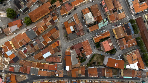 Top-down aerial view of an intricate network of narrow streets and old stone houses with reddish terracotta roofs, forming a classic Mediterranean urban pattern in a historic town center. Zenith shot.