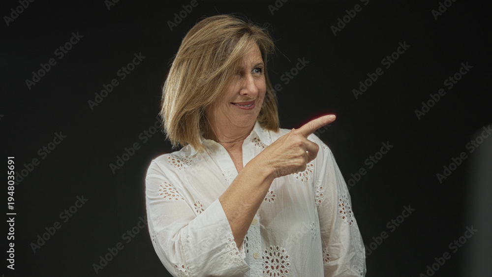 Fototapeta premium Woman in elegant white lace blouse smiling and pointing finger in studio with black background; confidence.