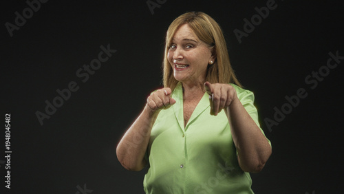 Cuadro en lienzo Middle age hispanic woman pointing fingers at camera, smiling and showing fingers in a green blouse in studio; playful confidence