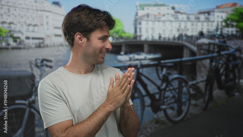 Photography Man with hands pressed together clapping on a street in amsterdam beside canal and bridge; contentment travel relaxation