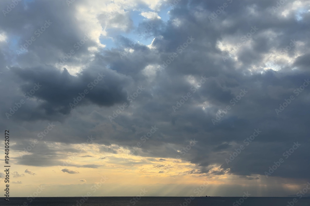 Fototapeta premium 厚い雲の隙間から差し込む光と夕方の空と水平線