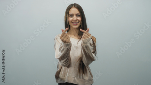 Bild auf Leinwand Teenage woman smiling showing double finger hearts with hands and braces, beige sweater in studio; playful