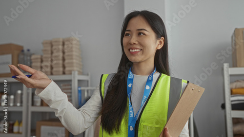 Fotografie Woman in a reflective vest holds a clipboard in a charity volunteer center, surrounded by supplies and boxes, embodying a conscientious spirit in an indoor community setting
