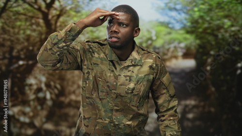 Soldier man shading hand to forehead while scanning a forest path for threats on patrol; vigilance duty.