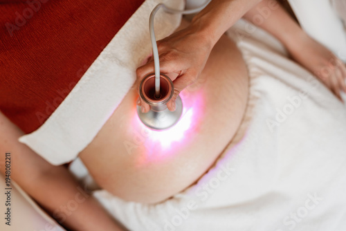 Professional aesthetician using a modern laser cavitation device on a female client for abdominal fat reduction and skin tightening in a medical spa setting.