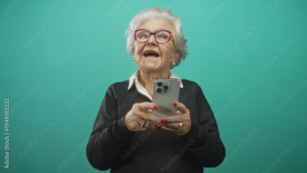 Fototapeta premium Senior woman holds smartphone with visible hands, mouth open and looking up in a studio; joyful curiosity.