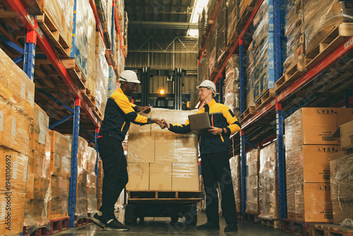Fotografie Two male workers shake hands as colleagues warehouse employees responsible for inspecting goods and operating forklift demonstrating teamwork and positive camaraderie at work among foreign workers