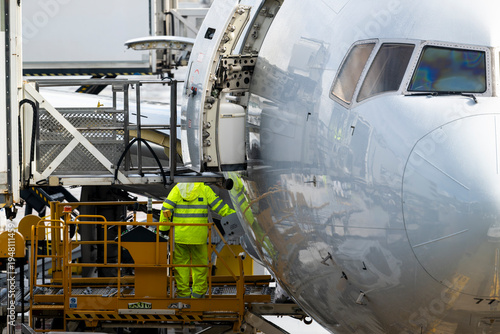 Airport ground crew operating cargo loading platform positioned at aircraft cargo door during airplane service operations at terminal gate.