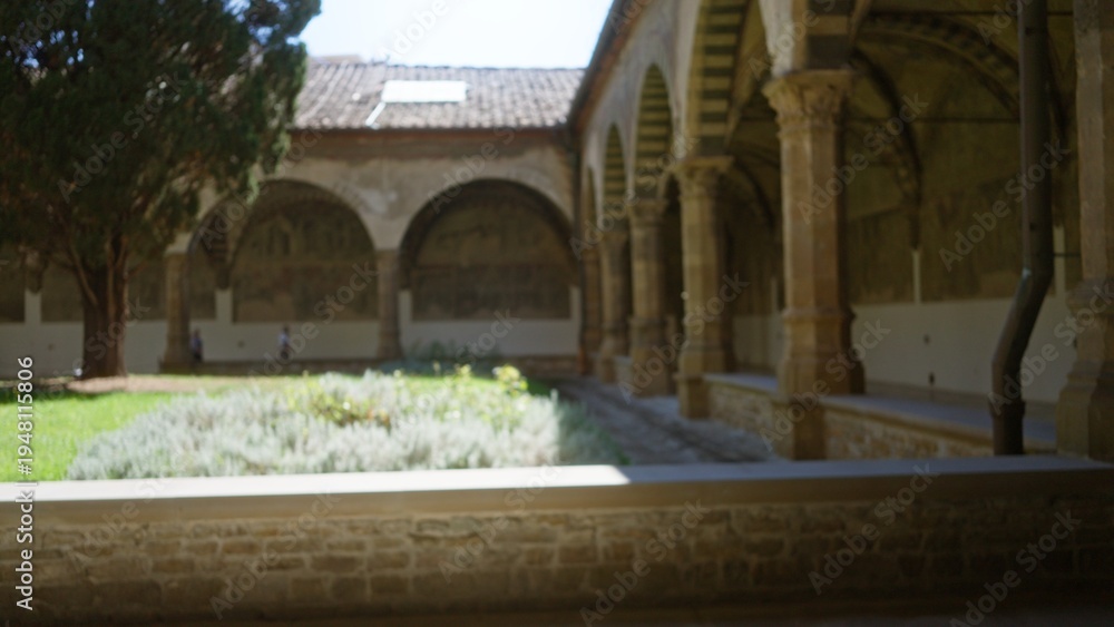 Fototapeta premium Historic cloister courtyard with arched colonnade and leafy garden in soft blurred focus, defocused; background backdrop copyspace template.