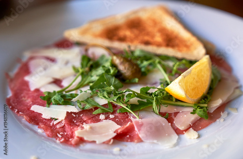 Carpaccio with slices of parmesan, toast and greenery with lemon