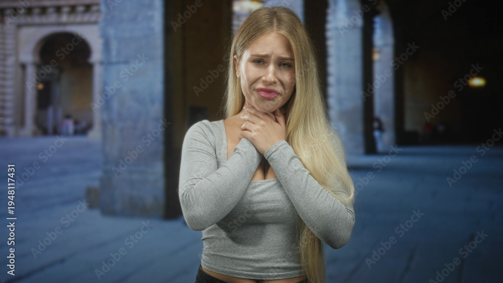 Fototapeta premium Woman clutching her neck with both hands in a stone archway building, choking and showing worried expression; distress fear vulnerability.