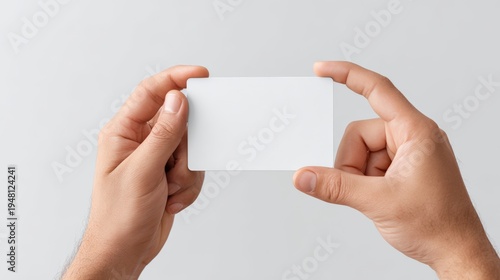 Hands holding a blank white card against a light gray background, suitable for business or personal branding, mockup for design purposes with copy space available
