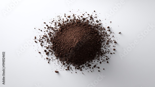 Ground coffee powder is scattered on a white surface, forming a textured mound with fine granules and larger particles, showcasing rich brown tones and a natural appearance