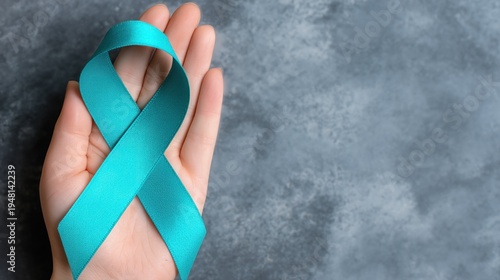 Turquoise Awareness Ribbon Held in Hand Against Gray Background