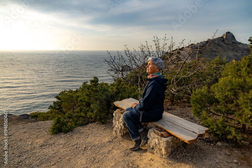 Elderly woman enjoying a scenic bench view overlooking the vast calm ocean during sunset hike
