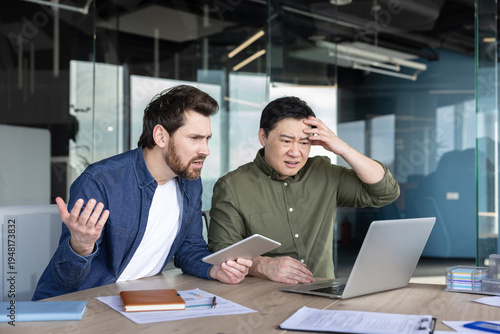 Fotografija Two businessmen at a modern office desk react with frustration and stress as a l