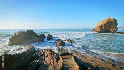 Penedo do Guincho at Praia da Santa Cruz in Portugal displays a rock arch with waves breaking on the coast. Visitors walk along the sandy beach enjoying the view of the ocean.