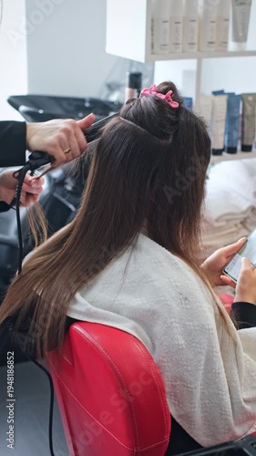 A hair stylist applies keratin treatment on a client's hair using a flat iron in a beauty salon. The process focuses on achieving smooth and straight hair.