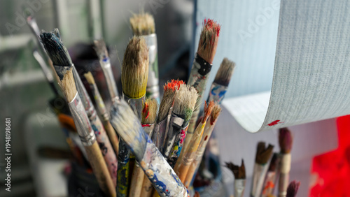 A pile of art brushes covered in paint. The brushes are standing in a tin