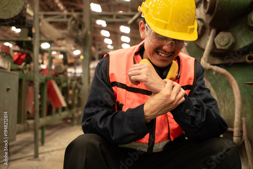 A worker wearing protective gear sits on the floor holding his injured wrist and expresses pain, emphasizing the importance of workplace safety and rapid response to accidents.