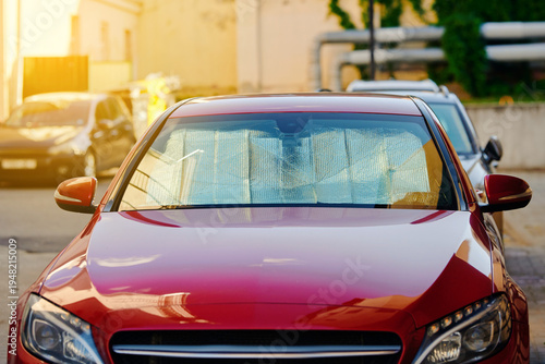 Obraz na plátně Front view of modern red car parked in an outdoor urban lot with reflective silver sunshade placed inside the windshield for heat and uv protection during bright sunny day