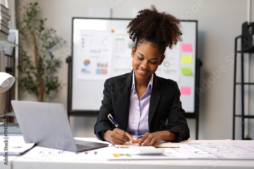 Smiling African American businesswoman, taking notes ideas for a new project while working in office.