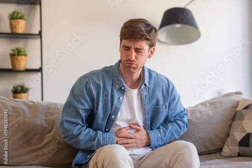 Fotografía Sick young man in pain holding belly stomach feeling hurt abdomen ache gastritis