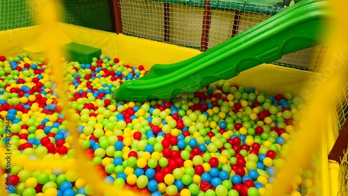 Photography bright indoor playground with colorful plastic ball pit and green slide, soft pl
