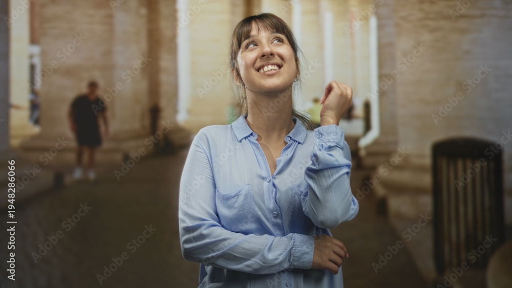Obraz premium Woman smiling with arms crossed and pointing finger amid stone columns in a building; joy reflection.