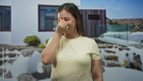 Принти на полотні Woman pinching nose in yellow t shirt at building entrance of house outdoors near glass railing; bad smell disgust reaction