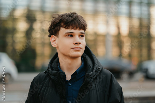 Closeup Young Man Thoughtful Gaze Near. Glass Facade Background, Neutral Expression, Soft Evening Light,