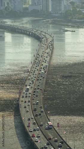 Cars traveling along the busy corredor sur, a critical highway bridge, with panama city's urban skyline against a hazy horizon and ocean mudflats at low tide - 4K  stock video